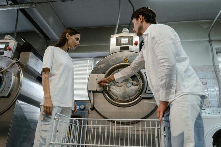 Man and woman operating industrial washing machines in a laundry facility.